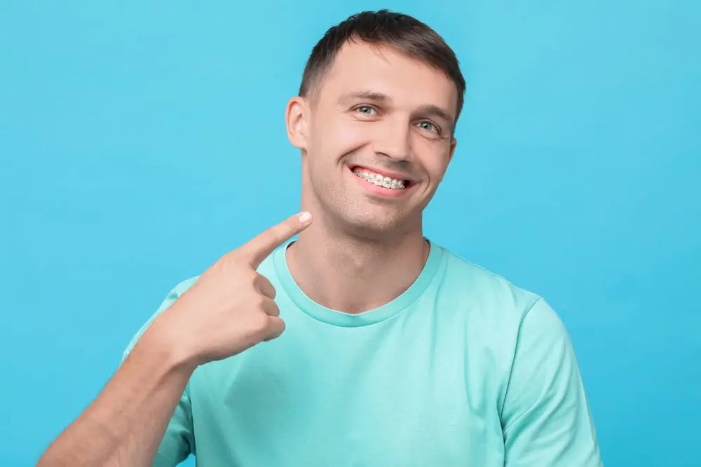 Man smiling and pointing at his braces against a blue background in NYC