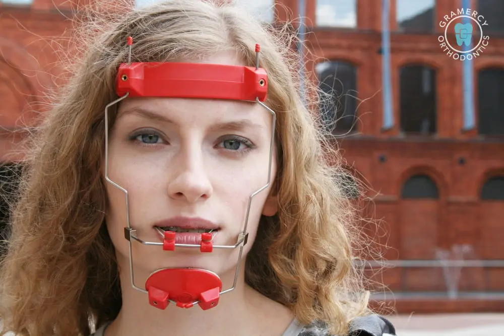 Person with wavy hair wearing a red Reverse Pull Headgear Braces in New York, NY, standing in front of red brick buildings.