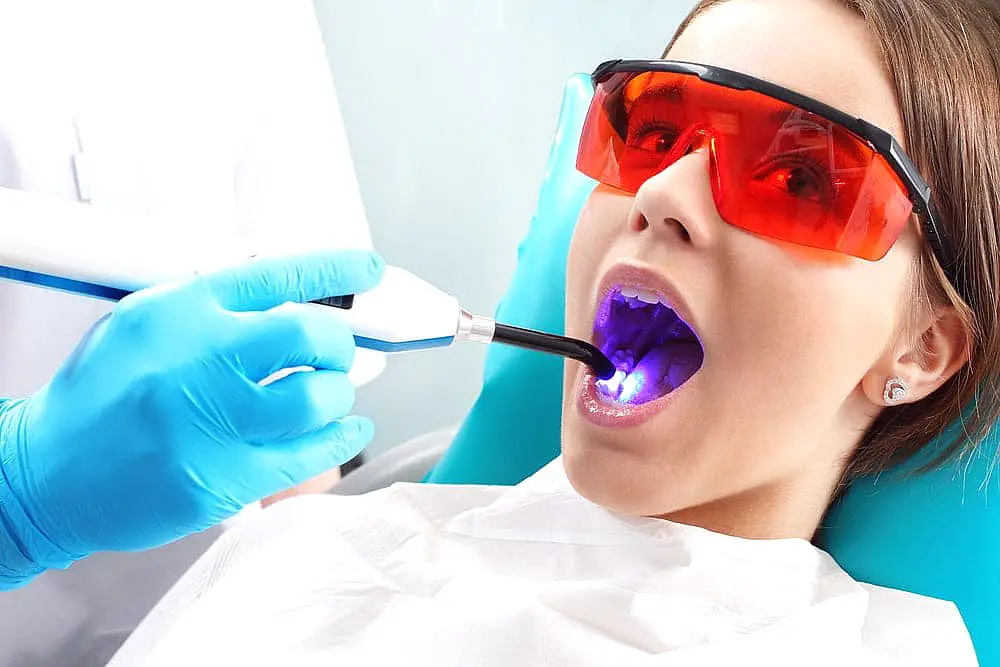 A patient wearing protective eyewear receives dental treatment with a UV light device while lying back in the dentist's chair, addressing concerns like tongue thrust in NYC