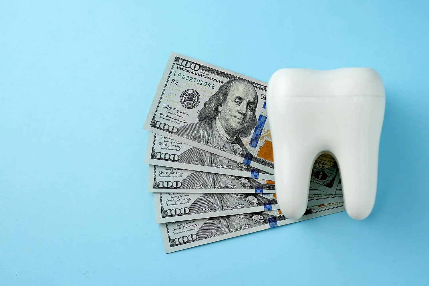 A large white tooth model is positioned beside several fanned-out $100 bills on a blue background, subtly highlighting the cost considerations of metal braces in NYC