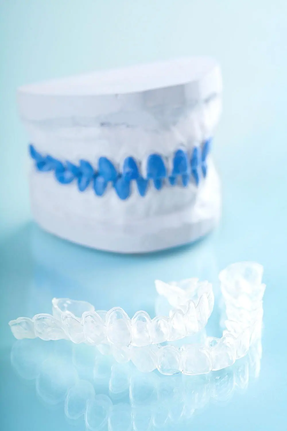 Clear dental aligners rest in front of a dental model with striking blue teeth against a serene light blue background, showcasing how Invisalign's payment plan makes achieving a perfect smile more accessible in NYC