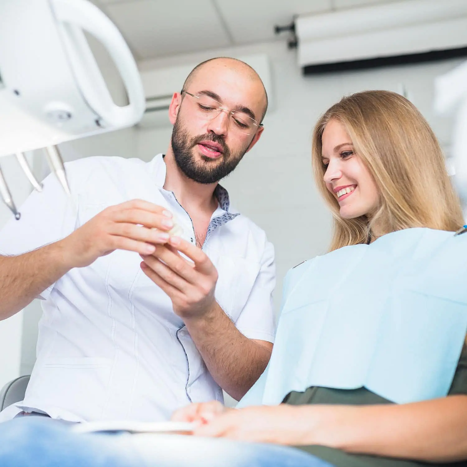 The dentist explained the dental model and showcased various orthodontic appliances to a smiling patient comfortably seated in the dental chair with a protective bib in NYC
