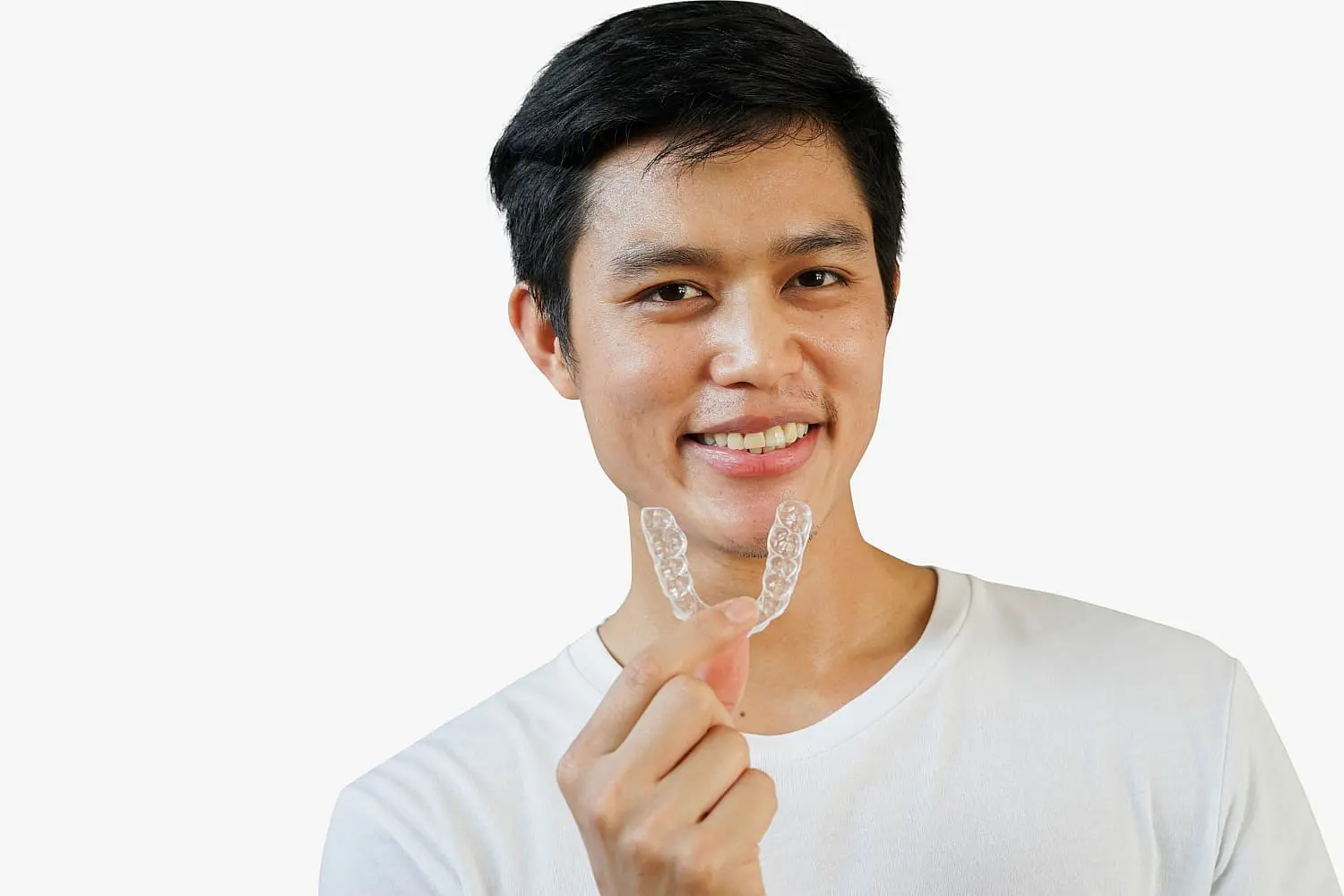 A person smiles while holding a clear dental retainer in their hand, showcasing the benefits of an Invisalign payment plan against a plain white background in NYC