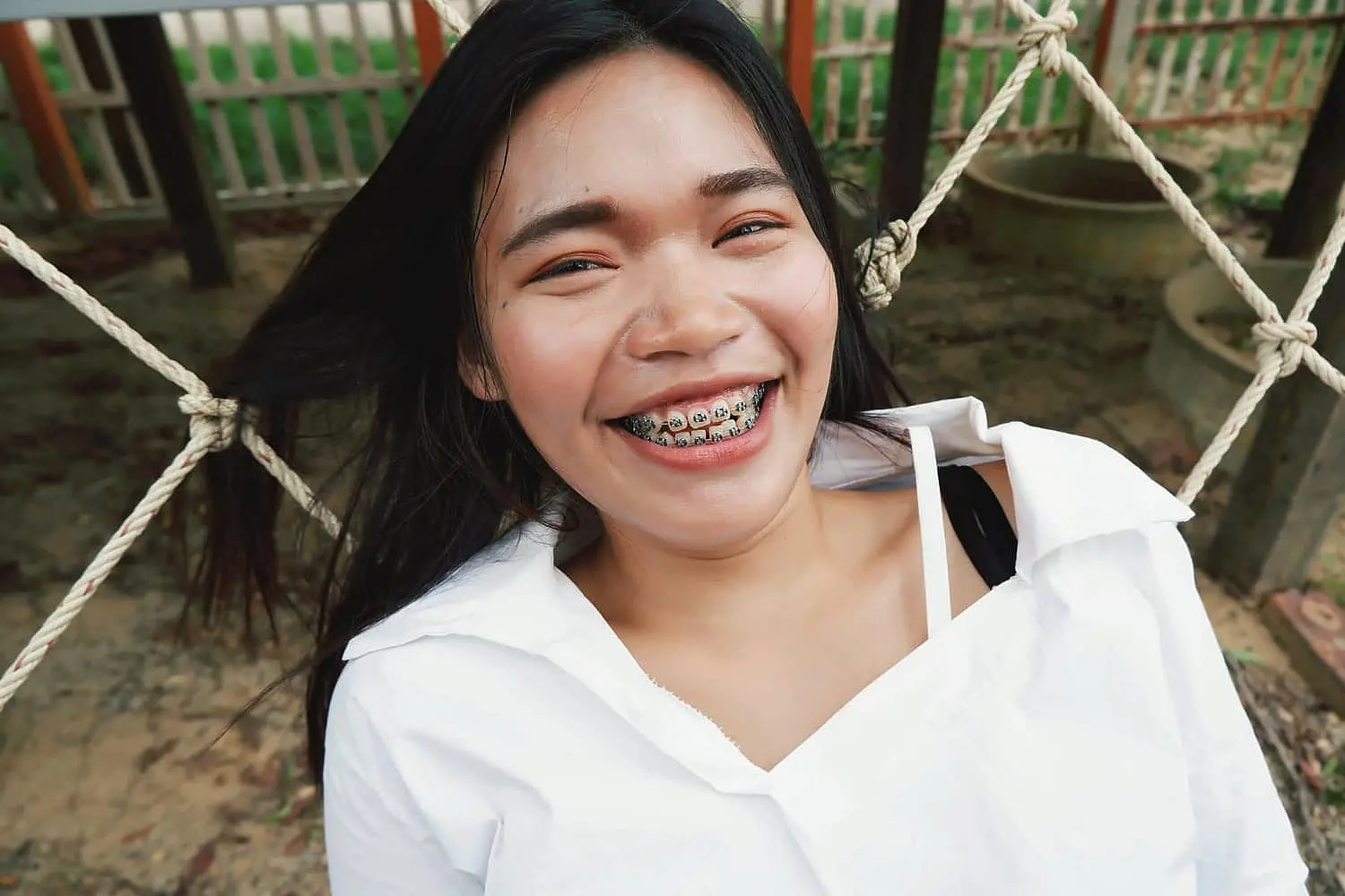 A cheerful individual showcasing their adult orthodontics, dressed in a white shirt, relaxes comfortably on a rope hammock in NYC