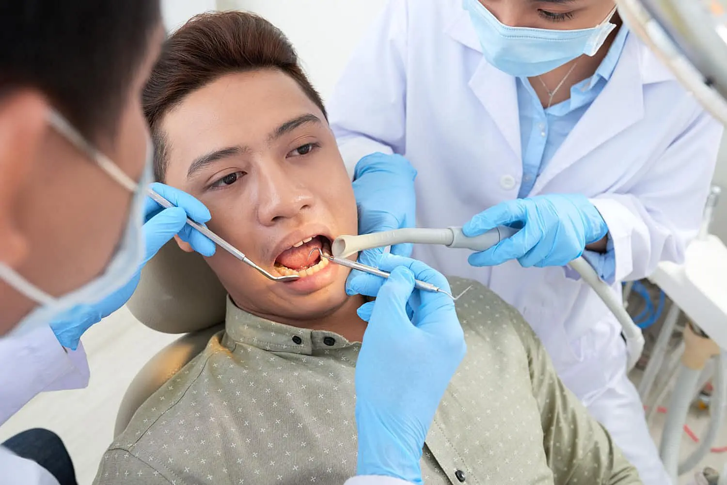 A patient with an overbite is receiving dental treatment from two dentists, both wearing masks and gloves in NYC