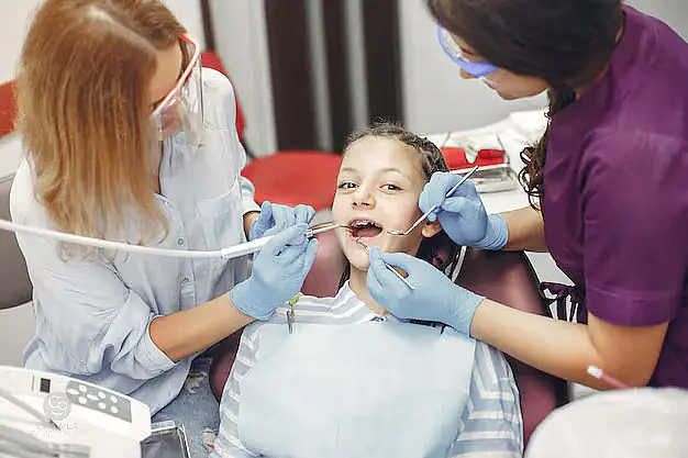 A child sits in a dental chair, surrounded by two attentive children's orthodontists carefully examining her teeth with precision dental instruments in NYC