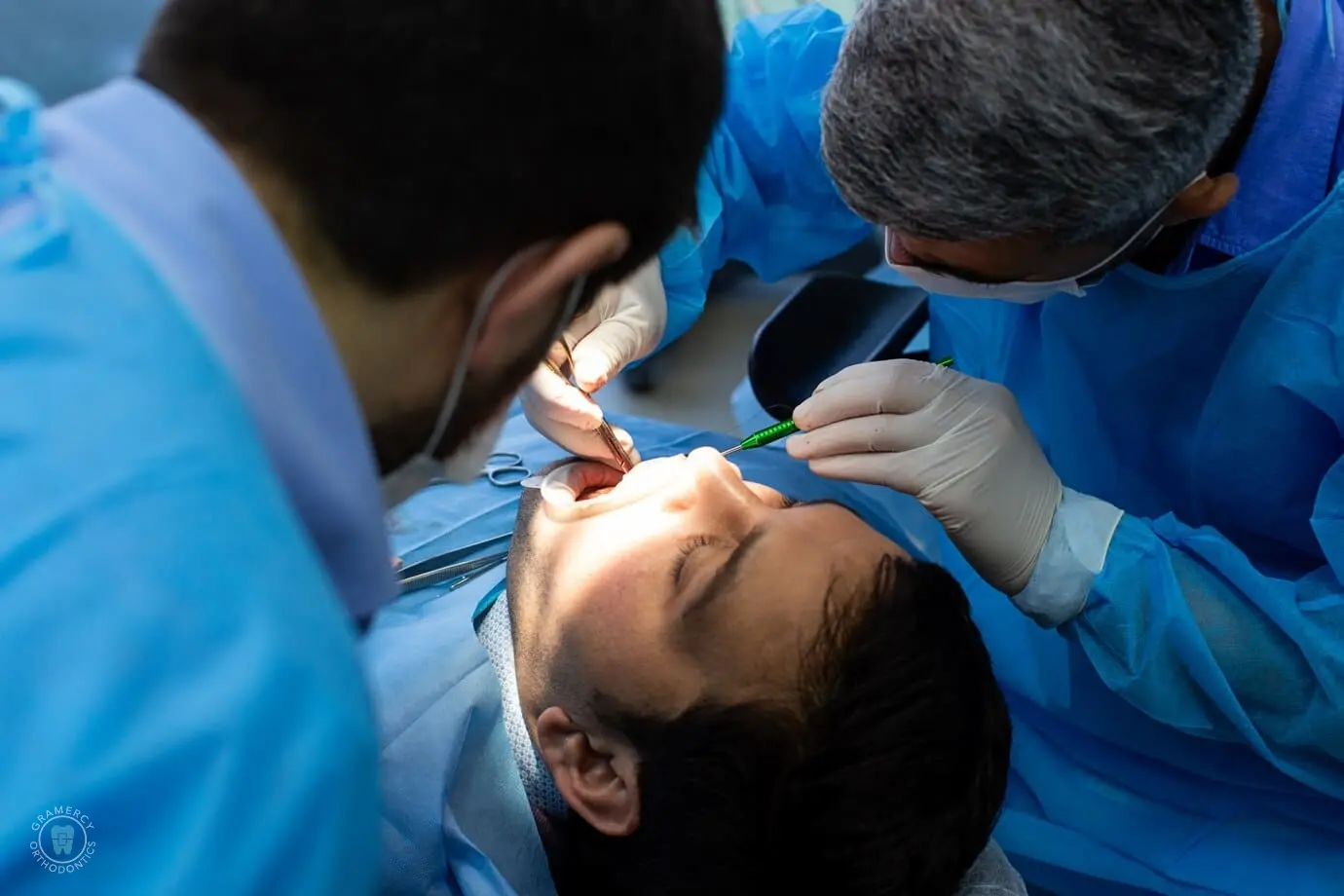 Dentist and assistant in blue scrubs carefully address a tongue thrust issue while performing a dental procedure on a patient reclining in the chair in NYC