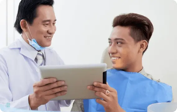 The dentist discusses jaw surgery options with a smiling patient, displaying detailed information on a tablet in the welcoming atmosphere of the dental clinic in NYC