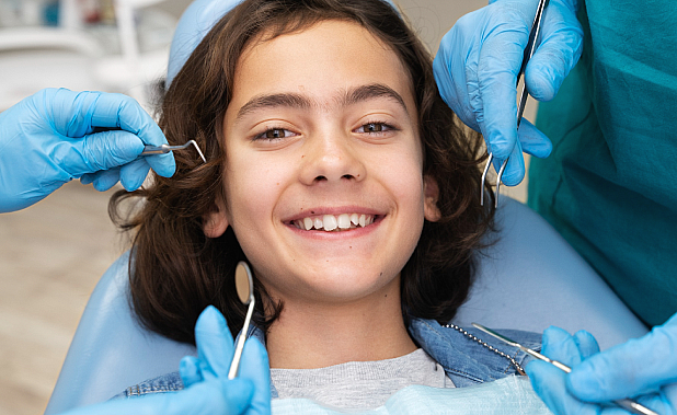 A young person beams with joy in a dental chair, surrounded by the gentle hands of children's orthodontists, expertly wielding their instruments in NYC
