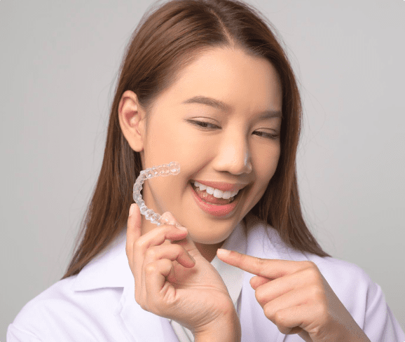 Person holding and pointing at a clear dental aligner, smiling, wearing a white coat in NYC