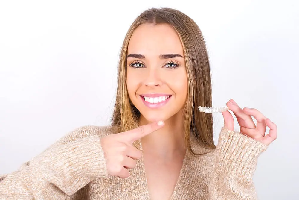 Person smiling and holding a clear dental aligner while pointing at it in NYC