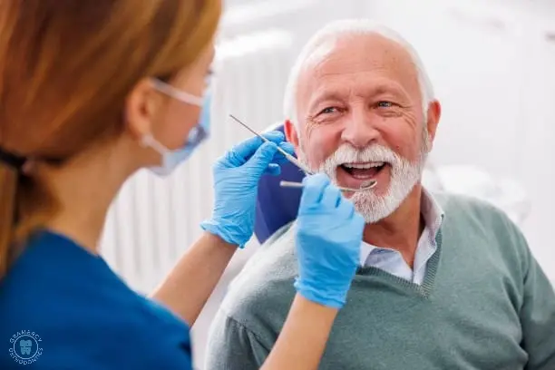 A dentist in a face mask and gloves examines a smiling elderly man, ensuring his teeth and gums are healthy post-jaw surgery in NYC