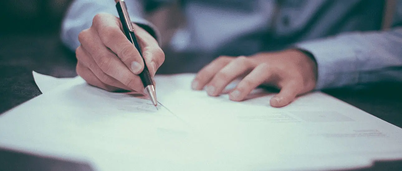 A person in a blue shirt writes on paper with a pen at a desk, possibly reviewing details about braces insurance in NYC