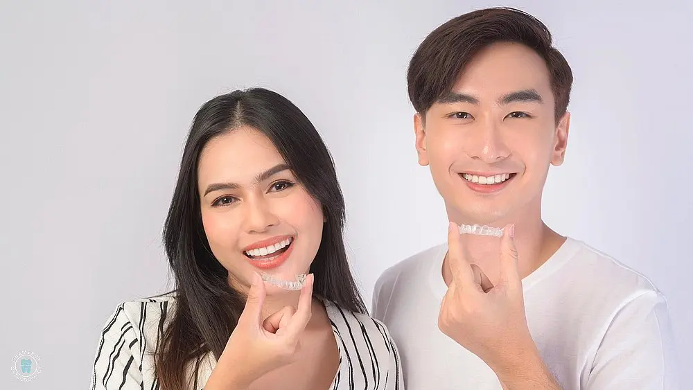 a young man and woman smiling while holding invisalign as one of the alternatives to braces in New York, NY