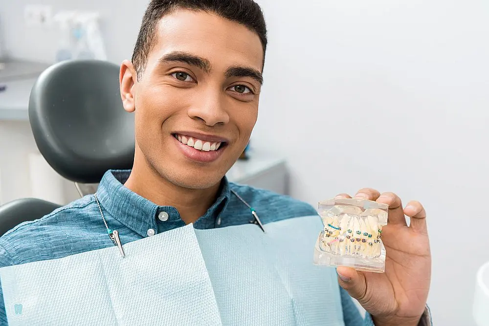 Smiling patient holding a dental model with clear aligners, showcasing how long do braces take in New York, NY discreetly.