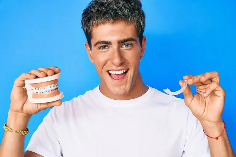 A man in a white shirt holds a dental model with braces and a clear aligner, smiling against a blue background, symbolizing the Invisalign vs Braces Cost in New York, NY.