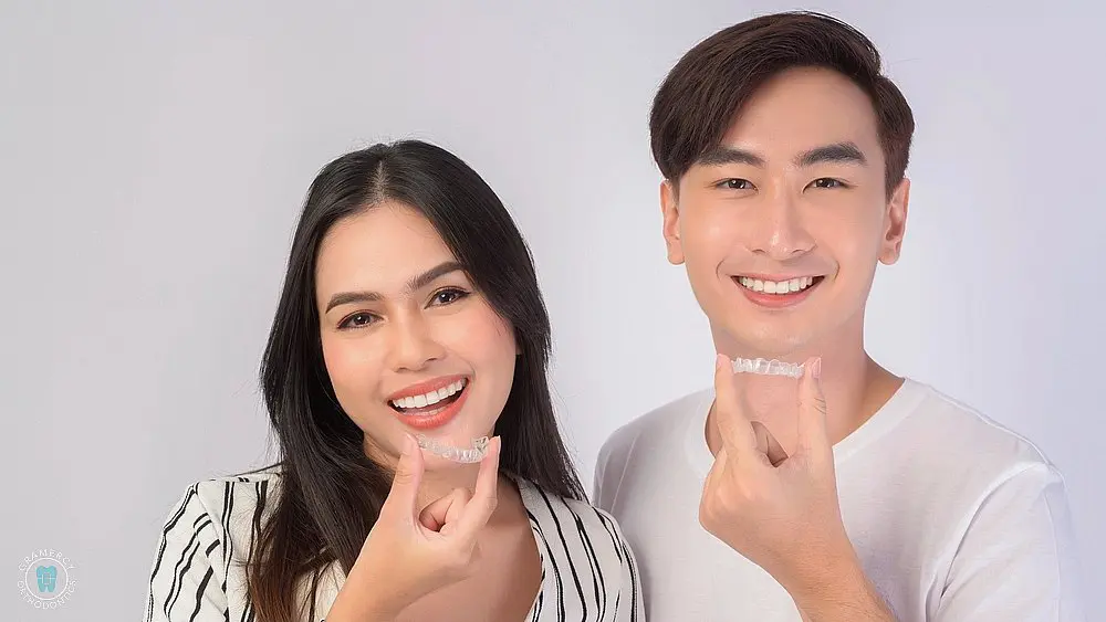 young smiling man and woman holding invisalign clear aligners braces white background - Can Invisalign Fix Overbite in New York, NY.