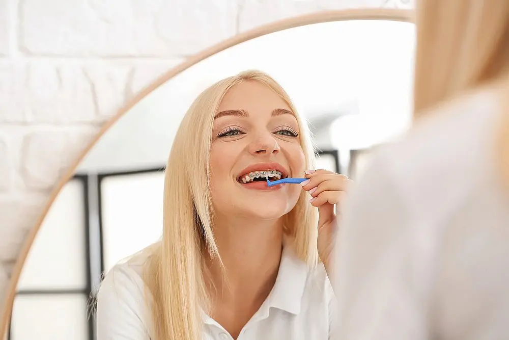 young woman metal braces toothbrush home - How to Floss with Braces in New York, NY