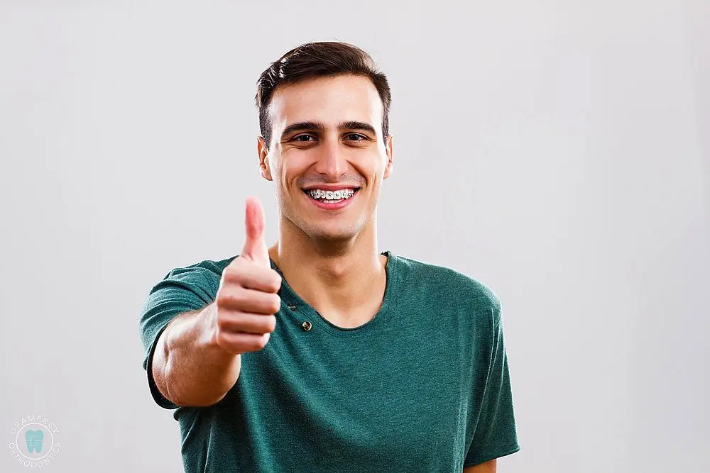 man with metal braces showing thumbs up - How To Get Braces Glue Off Teeth in New York CIty, NY 