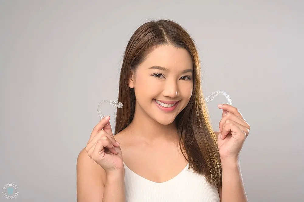 young smiling woman holding invisalign clear aligners white background studio dental - How Does Invisalign Work in New York City, NY 