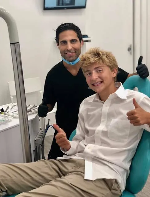 At Gramercy Orthodontics in New York, NY, Dr. Barry Elaahi and a smiling teen patient in a dental chair give thumbs up.