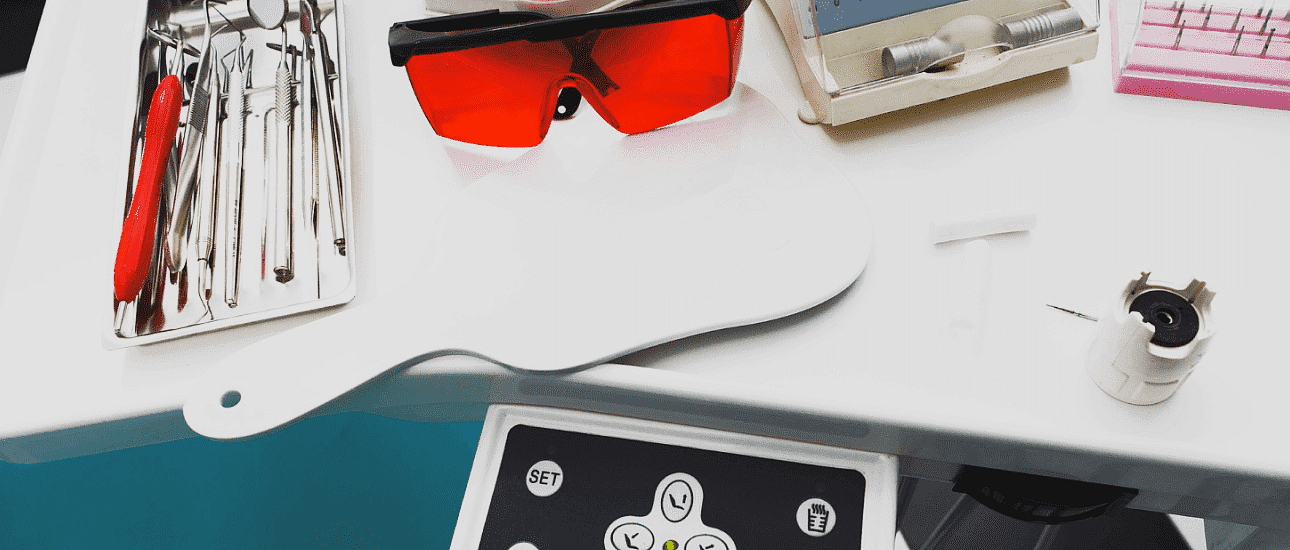 Dental equipment on a table includes tools, metal braces, red protective glasses, a small mirror, and a control panel in NYC
