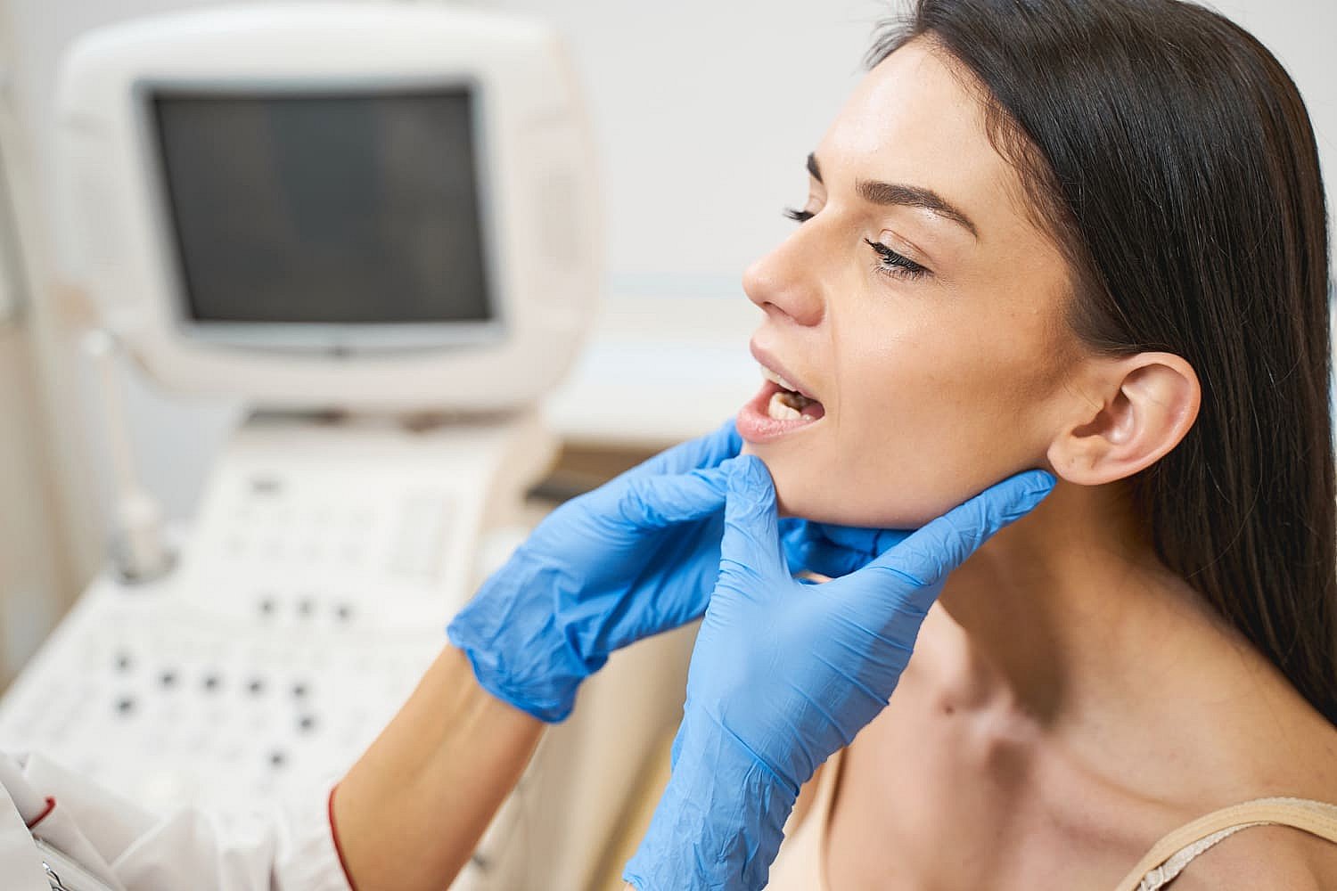 A healthcare professional, donning blue gloves, examines a patient's throat. With the patient's mouth open wide, it almost looks like a preparatory step for jaw surgery in NYC