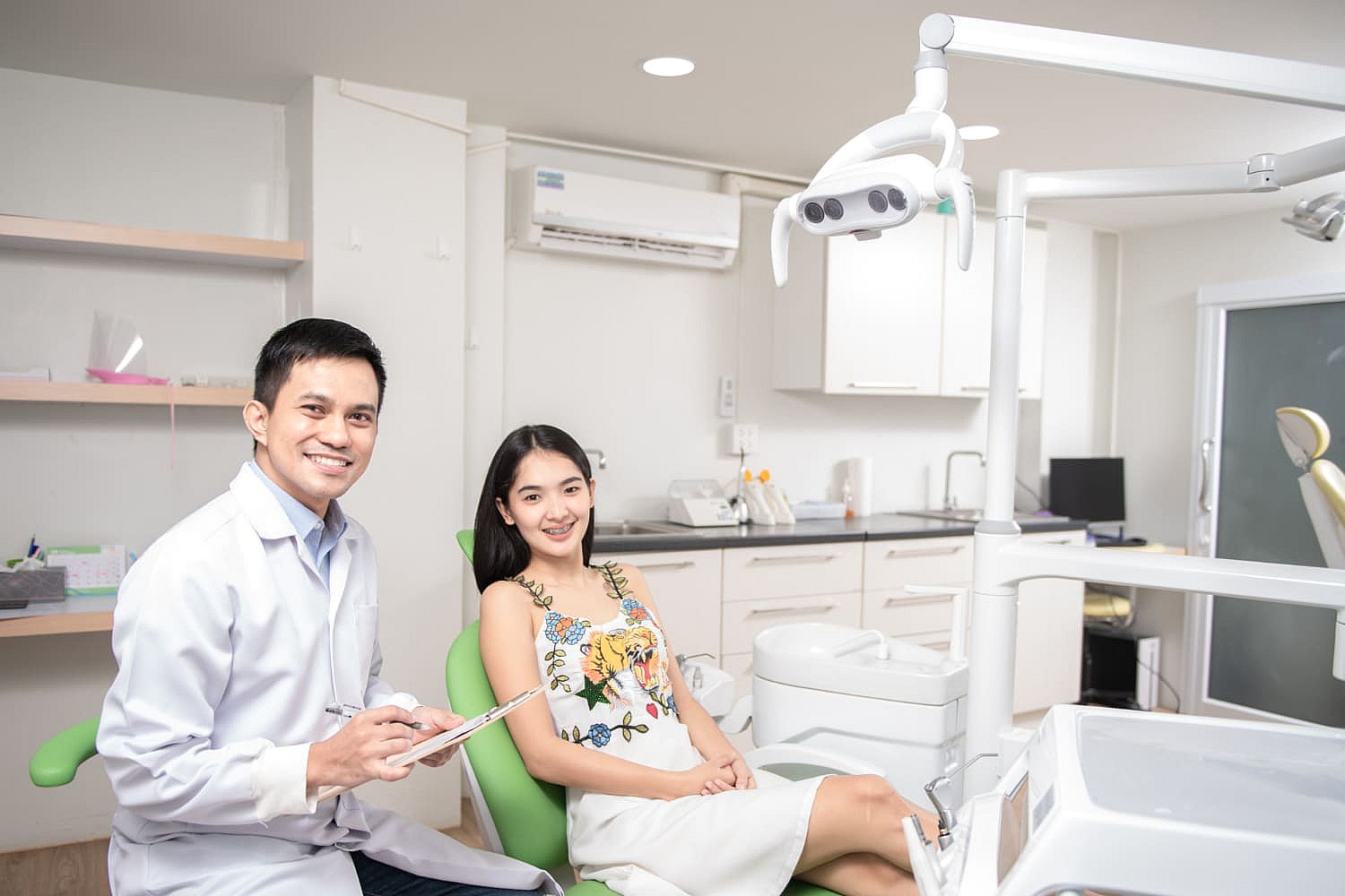 A dentist from Orthodontic Experts, wearing a white coat, is seated next to a patient in a dental clinic. The patient smiles confidently in the dental chair, surrounded by state-of-the-art dental equipment in NYC