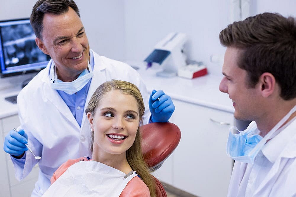 A dentist consults with a smiling female patient in a dental chair, discussing the benefits of a Herbst Appliance, while a dental assistant observes in NYC