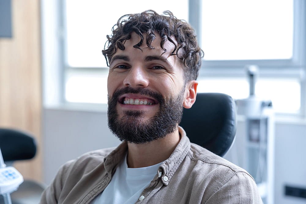 Smiling man with curly hair and a beard comfortably sits in a dental office chair, exploring his options for adult orthodontics in NYC