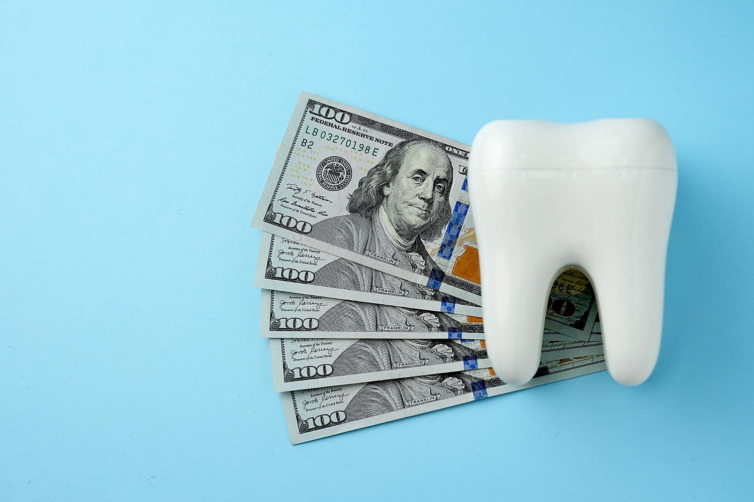 A large white tooth model is positioned beside several fanned-out $100 bills on a blue background, subtly highlighting the cost considerations of metal braces in NYC