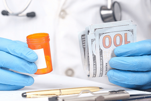 A person in a lab coat holds a pill bottle in one hand and a stack of hundred-dollar bills in the other, hinting at decisions beyond just prescriptions. On the table lies a stethoscope and pen, perhaps next to an Invisalign payment plan pamphlet in NYC