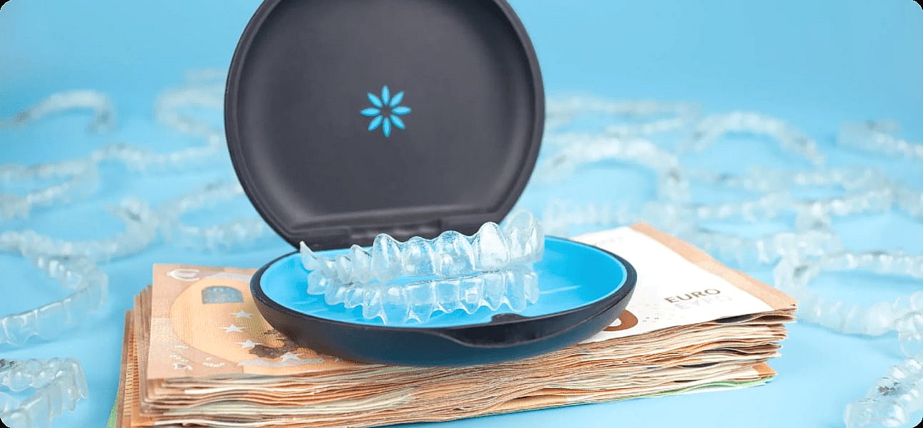 Clear dental aligners in an open case rest atop a stack of euro banknotes, symbolizing the Invisalign cost, while more aligners are scattered in the background in NYC