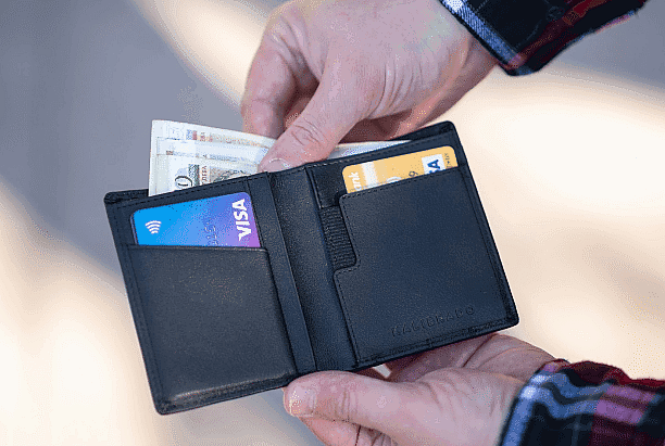 Hands holding an open wallet reveal a Visa card, another card, and multiple banknotes. It's clear the owner is ready for anything—be it groceries, gifts, or even keeping up with their Invisalign Payment Plan in NYC