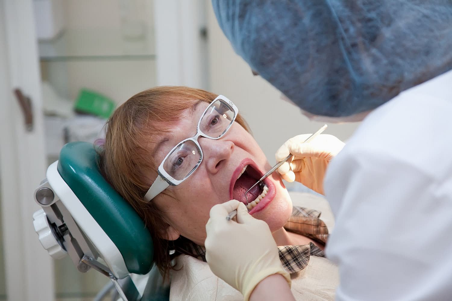 A dentist examines a patient's open mouth, using dental tools to assess the effects of tongue thrust on oral health in NYC