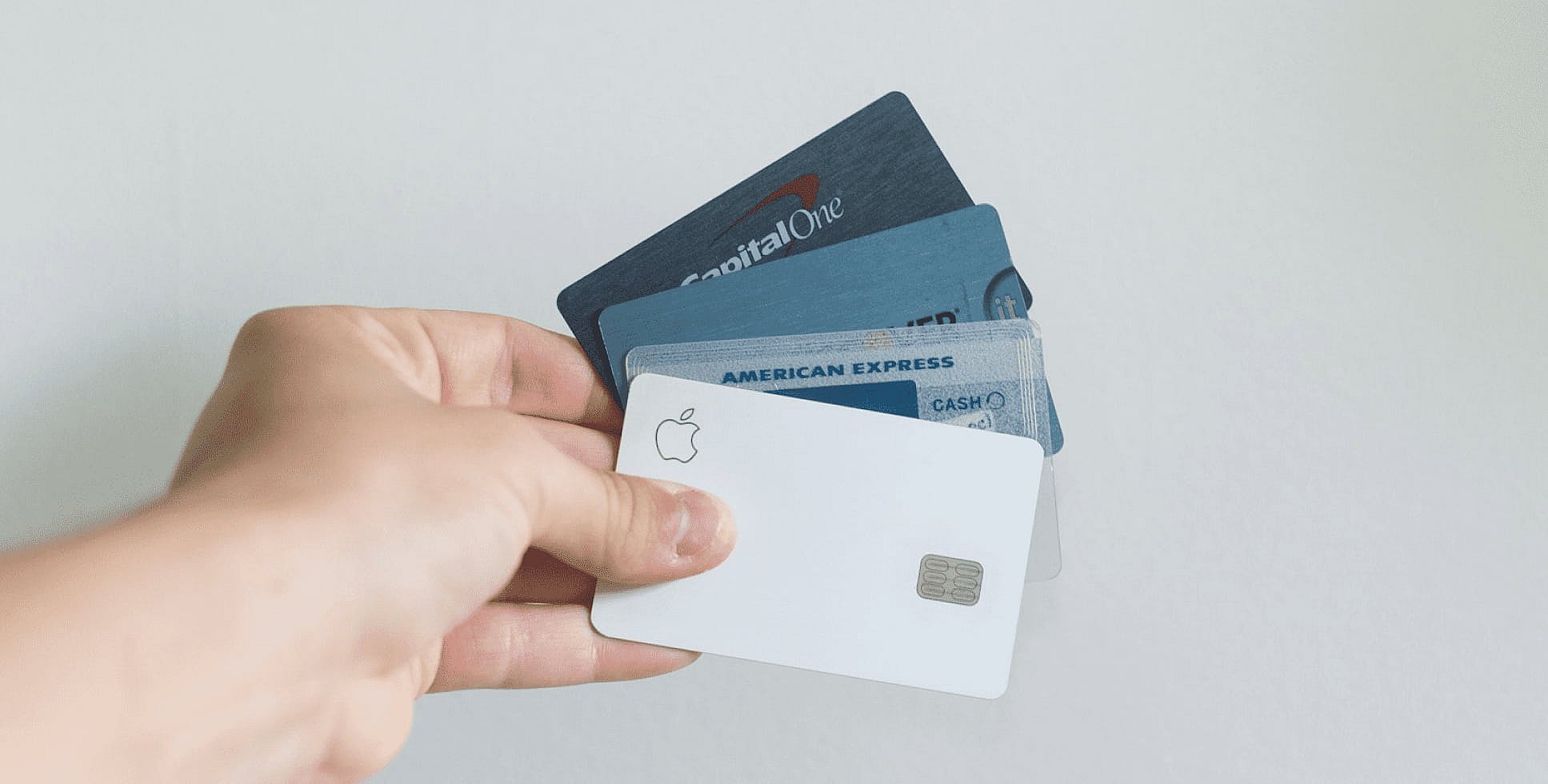 A hand holds a fan of credit cards, featuring Apple, Capital One, and American Express. Perfect for managing expenses like an Invisalign payment plan against a plain background in NYC