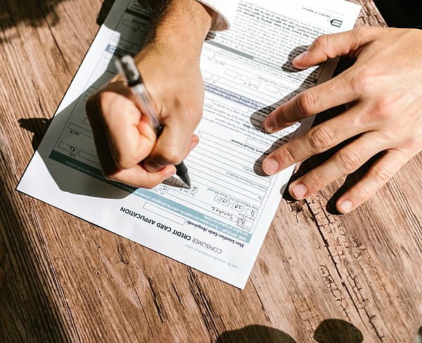 A person is diligently filling out a business credit card application on a wooden table, pondering whether Invisalign might be covered by insurance in NYC