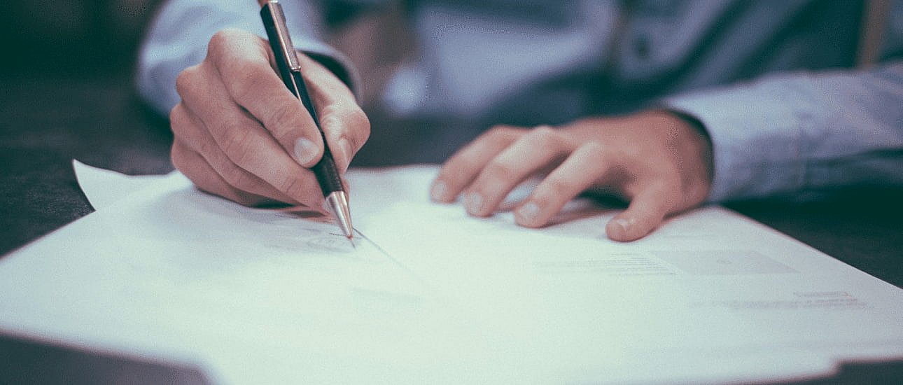 A person in a blue shirt writes on paper with a pen at a desk, possibly reviewing details about braces insurance in NYC