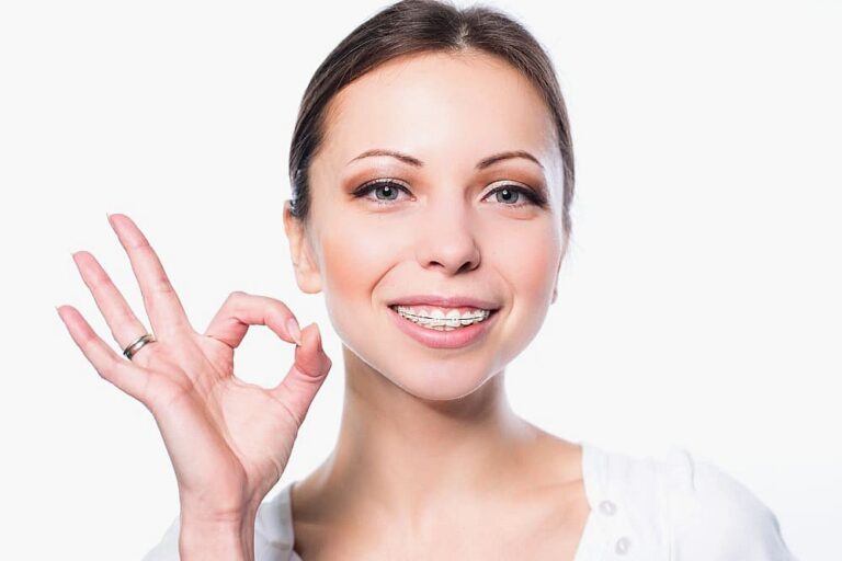 Woman with straight brown hair smiles while showing a hand gesture for "okay." She is care clear braces at Gramercy Orthodontics in NYC